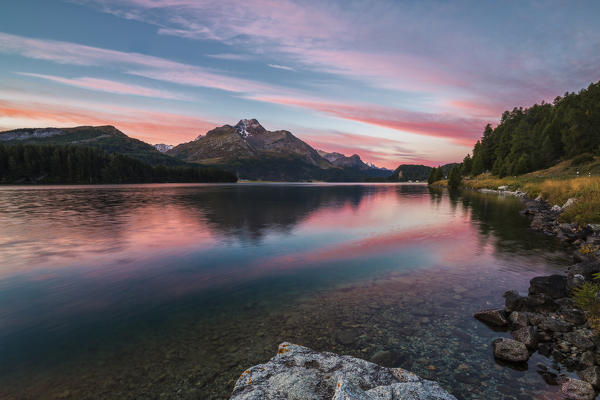Pink sky at dawn illuminates the peaks reflected in Lake Sils Engadine Canton of Graubünden Switzerland Europe