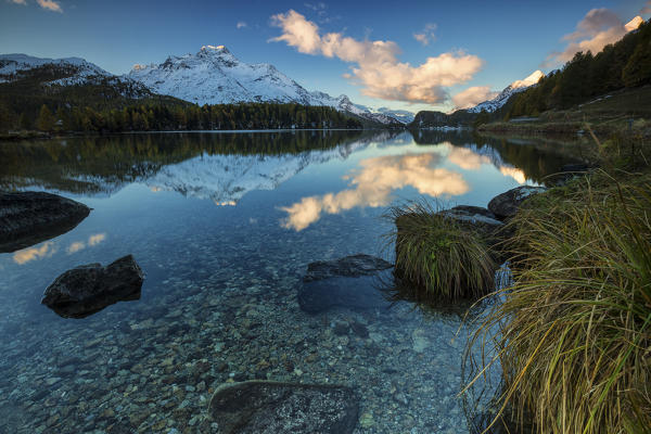 Dawn illuminates the peaks reflected in the calm waters of Lake Sils Engadine Canton of Graubünden Switzerland Europe