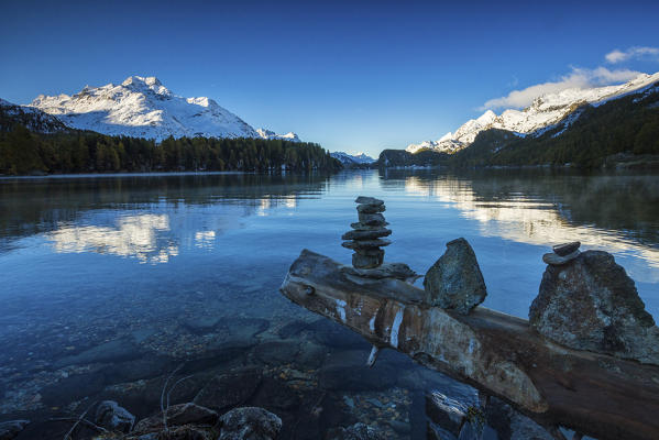 Dawn illuminates the peaks reflected in the calm waters of Lake Sils Engadine Canton of Graubünden Switzerland Europe