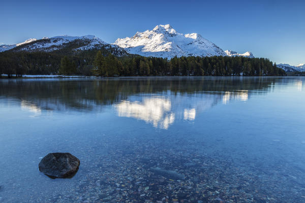 Dawn illuminates the peaks reflected in the calm waters of Lake Sils Engadine Canton of Graubünden Switzerland Europe