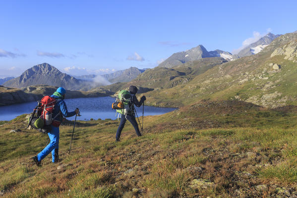 Hikers admire the peaks and the blue alpine lake Minor Valley High Valtellina Livigno Lombardy Italy Europe