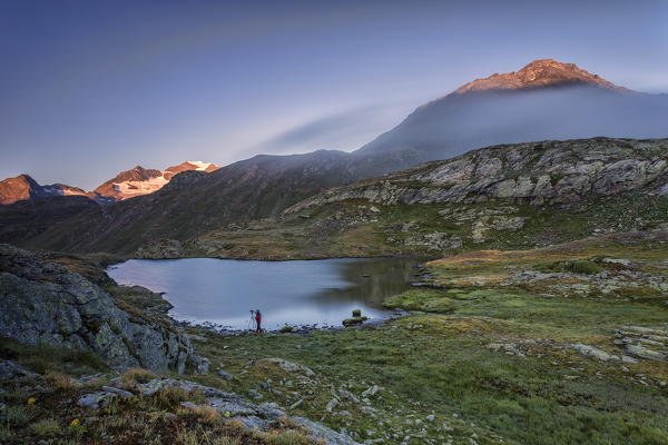 Photographer in action on the shore of the alpine lake at dawn Minor Valley High Valtellina Livigno Lombardy Italy Europe