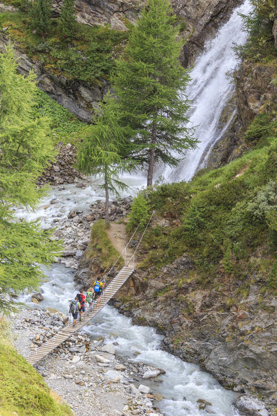 Hikers cross the wooden bridge on a creek in the woods Minor Valley High Valtellina Livigno Lombardy Italy Europe