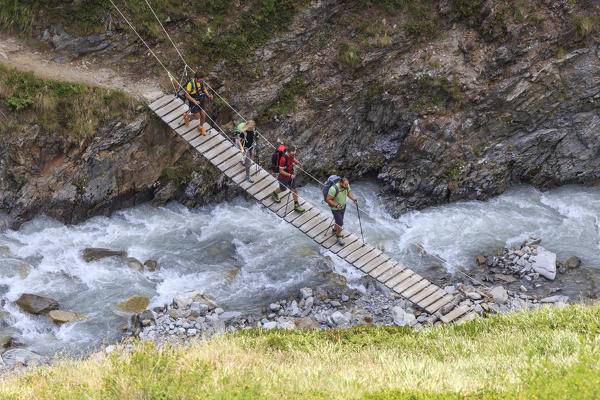 Hikers cross the wooden bridge on a creek Minor Valley High Valtellina Livigno Lombardy Italy Europe