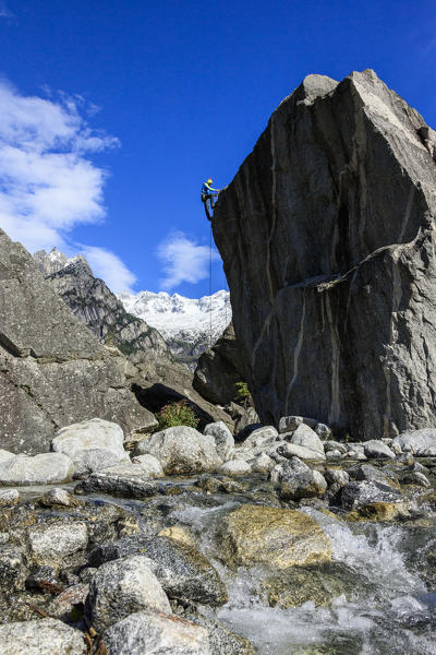 Climber on steep rock face in the background blue sky and snowy peaks of the alps Masino Valley Valtellina Lombardy Italy Europe