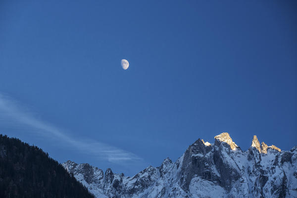 The moon on the snowy mountains illuminates the peaks at sunset Bondasca Valley Switzerland Europe
