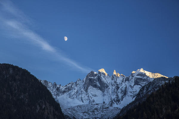 The moon on the snowy mountains illuminates the peaks at sunset Bondasca Valley Switzerland Europe