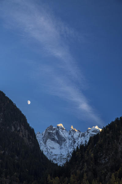 The moon on the snowy mountains illuminates the peaks at sunset Bondasca Valley Switzerland Europe