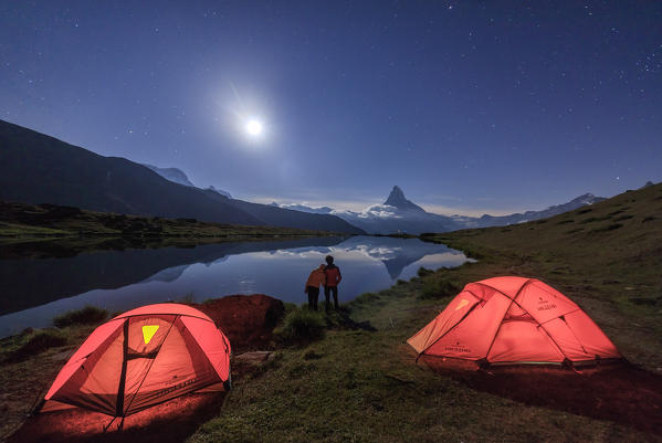 Lovers admire Matterhorn reflected in Lake Stellisee on a starry night of full moon Zermatt Valais Switzerland Europe