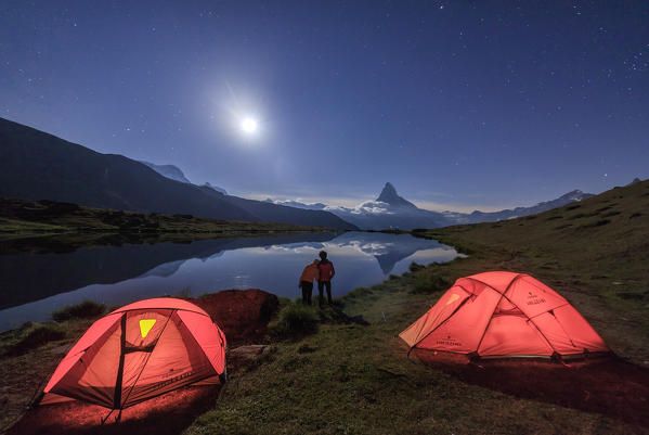 Lovers admire Matterhorn reflected in Lake Stellisee on a starry night of full moon Zermatt Valais Switzerland Europe