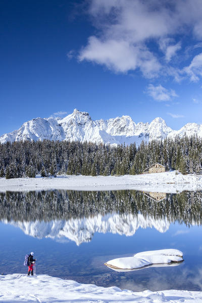 Hiker admires the snowy peaks and woods reflected in Palù Lake Malenco Valley Valtellina Lombardy Italy Europe