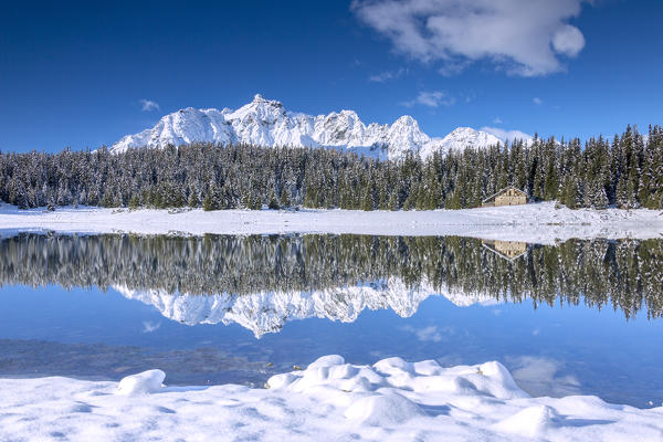 Wooden chalet surrounded by snowy peaks and woods reflected in Palù Lake Malenco Valley Valtellina Lombardy Italy Europe