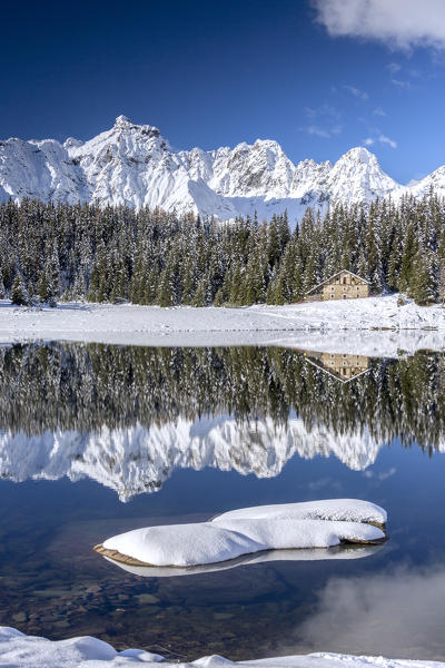 Wooden chalet surrounded by snowy peaks and woods reflected in Palù Lake Malenco Valley Valtellina Lombardy Italy Europe