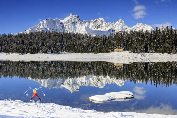 Hiker jumps on the shore of 
Palù Lake surrounded by snowy peaks and woods Malenco Valley Valtellina Lombardy Italy Europe