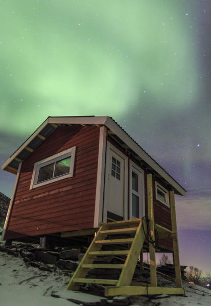 The Northern Lights illuminates the wooden cabin Oteren Storfjorden Lyngen Alps Tromsø Lapland Norway Europe