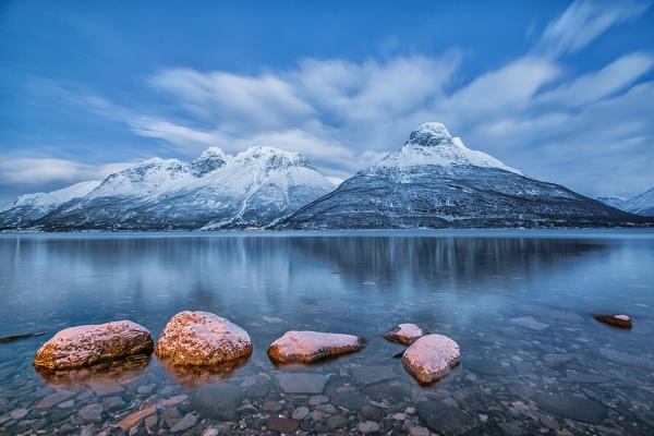 Blue sky at dusk and snowy peaks are reflected in the frozen sea at Oteren Storfjorden Lapland Lyngen Alps Tromsø Norway Europe