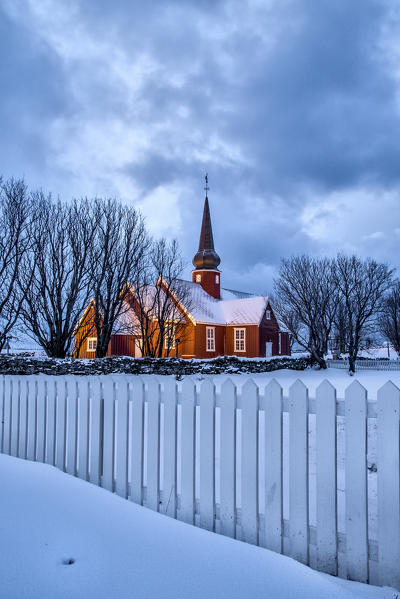 The illuminated church at dusk in the cold snowy landscape at Flakstad Lofoten Norway Europe