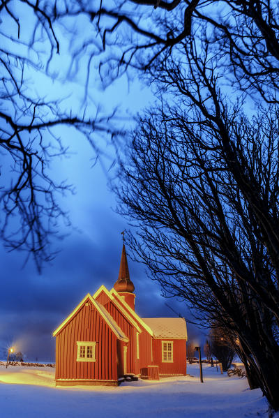 Lights on the church at dusk with the snowy peaks in the background Flakstad Lofoten Islands Norway Europe