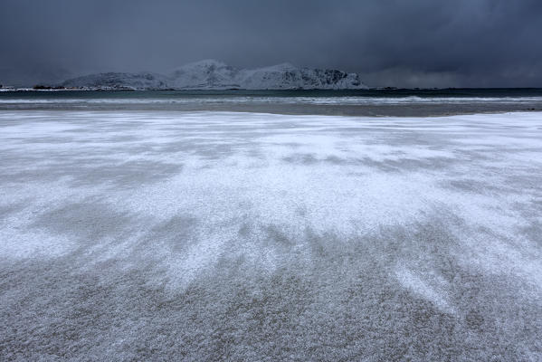 Waves of the icy sea on the beach in the background the snowy peaks Ramberg Lofoten Islands Norway Europe