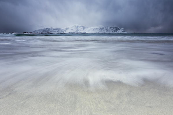 Waves of the icy sea on the beach in the background the snowy peaks Ramberg Lofoten Islands Norway Europe