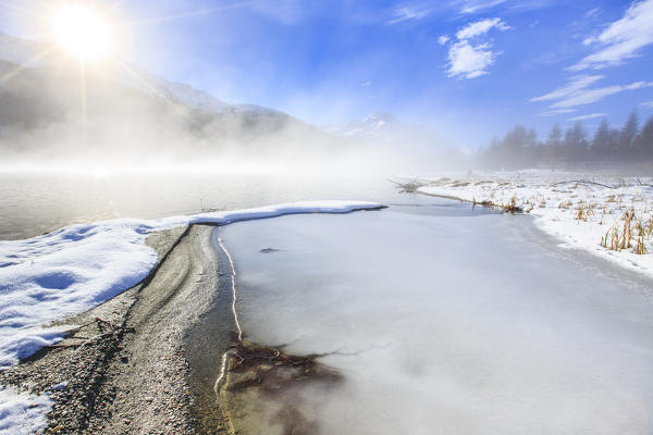 Winter sun light up the frozen Lake Silvaplana surrounded by mist Maloja Canton of Graubünden Engadine Switzerland Europe