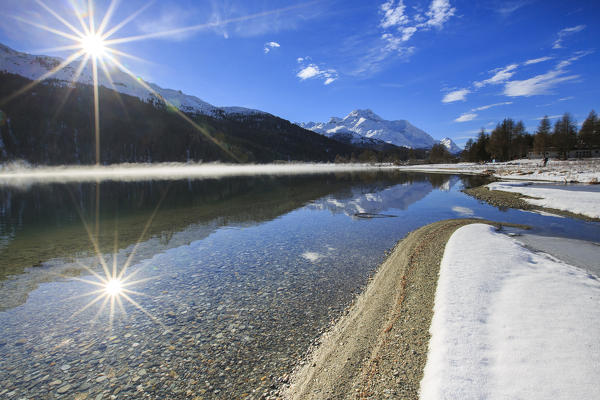Rays of winter sun illuminate Lake Silvaplana still partially frozen Maloja Engadine Graubunden Canton Switzerland Europe