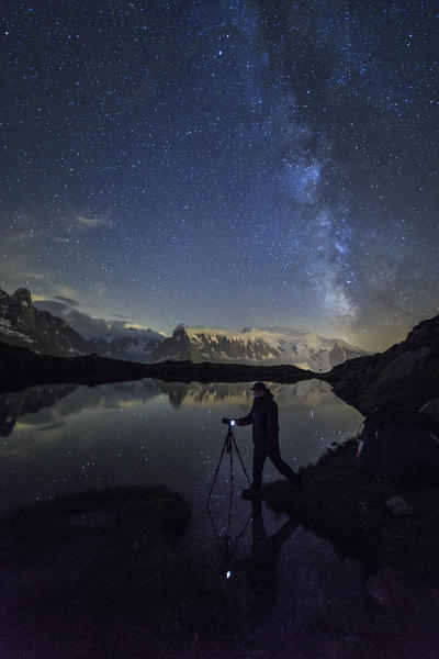 Photographer under starry sky and Milky Way reflected on Lac de Cheserys Chamonix Haute Savoie France Europe