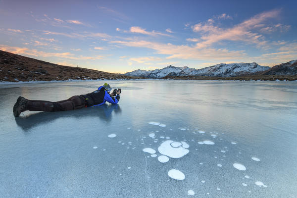 Photographer in action on the frozen surface of Andossi Lake at sunrise Spluga Valley Valtellina Lombardy Italy Europe