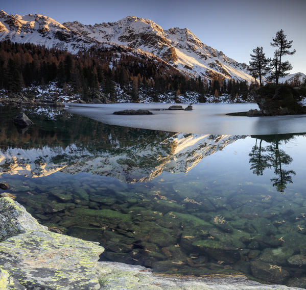 Autumn reflections at Saoseo Lake still partially frozen Poschiavo Valley Canton of Graubuenden Switzerland Europe