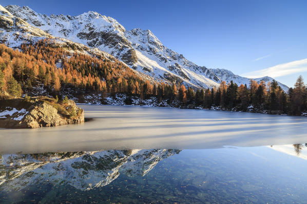 Autumn reflections at Saoseo Lake still partially frozen Poschiavo Valley Canton of Graubuenden Switzerland Europe