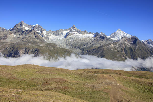 Green pastures and blue sky frame the high peak of Dent Herens Gornergrat Canton of Valais Switzerland Europe