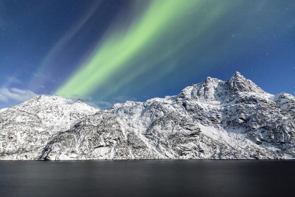 Northern Lights illuminate the snowy peaks and the blue sky during a starry night Budalen Svolvaer Lofoten Islands Norway Europe