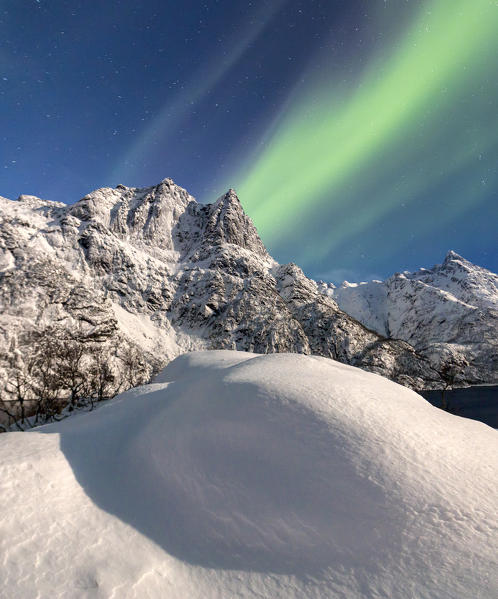 Northern Lights illuminate the snowy peaks and the blue sky during a starry night Budalen Svolvaer Lofoten Islands Norway Europe