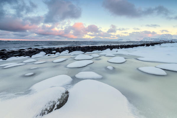 Dawn on the cold sea surrounded by snowy  rocks shaped by wind and ice at Eggum Vestvagøy Island Lofoten Islands Norway Europe