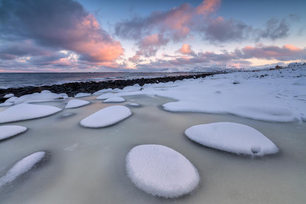 Dawn on the cold sea surrounded by snowy  rocks shaped by wind and ice at Eggum Vestvagøy Island Lofoten Islands Norway Europe