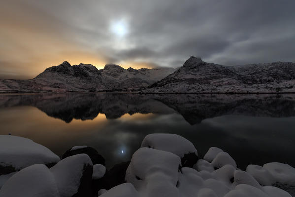The light of the moon and the snowy peaks are reflected in the cold sea at Svolvaer Lofoten Islands Norway Europe