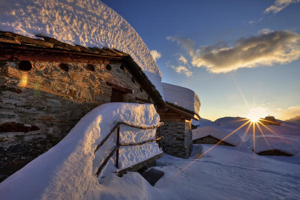 Sunset on Alpe Prabello. A small group of huts crushed by the weight of snow in winter. Valmalenco. Valtellina Lombardy. Italy Europe