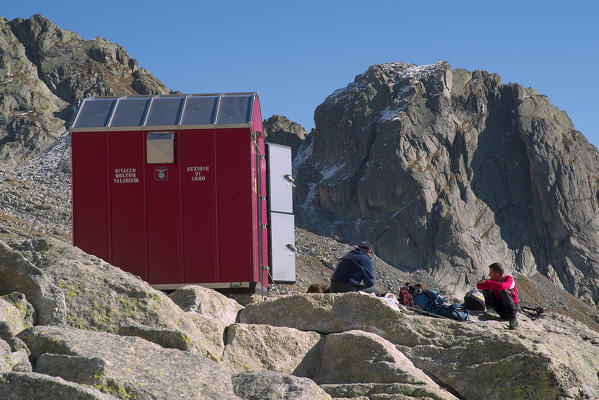 Hikers resting at the entrance of the bivouac Molteni Valsecchi makeshift shelter for trekkers who venture on these  peaks. Valmasino. Valtellina. Lombardy Italy Europe