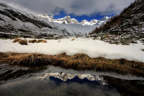 Pizzo Cengalo and Gemelli are reflected in a pool clear of snow in Val Porcellizzo. Valmasino Valtellina. Lombardy Italy Europe