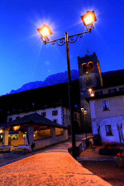 The lights come on at dusk in the central Kuerc square in the village of Bormio. In the background the Alberti Tower. Valtellina. Lombardy. Italy Europe