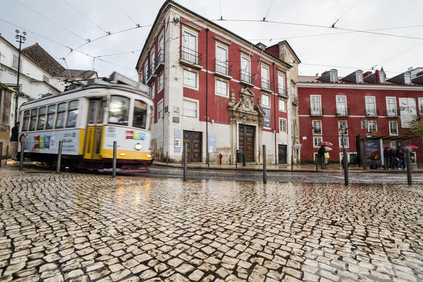 Yellow tram number 28 passes in Alfama district characterized by a typical architecture on a rainy day Lisbon Portugal Europe