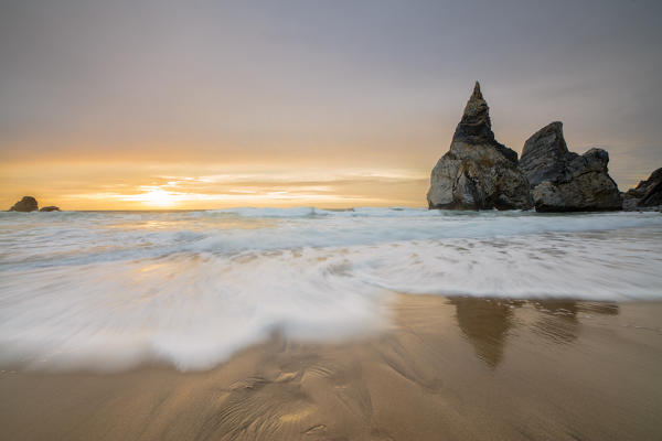 Ocean waves crashing on the beach of Praia da Ursa at sunset surrounded by cliffs Cabo da Roca Colares Sintra Portugal Europe