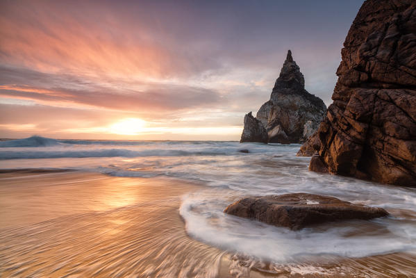 Golden reflections of the cliffs on Praia da Ursa beach bathed by ocean at sunset Cabo da Roca Colares Sintra Portugal Europe