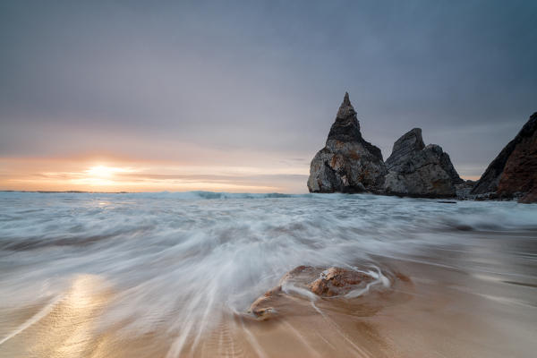 Ocean waves crashing on the beach of Praia da Ursa at sunset surrounded by cliffs Cabo da Roca Colares Sintra Portugal Europe