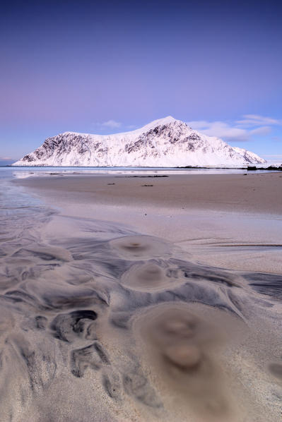 Pink sky and snowy peaks frame the surreal Skagsanden beach at sunset Flakstad Nordland county Lofoten Islands Norway Europe