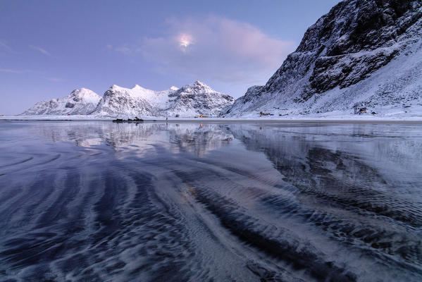 Waves and ice on the surreal Skagsanden beach surrounded by snowy peaks Flakstad Nordland county Lofoten Islands Norway Europe