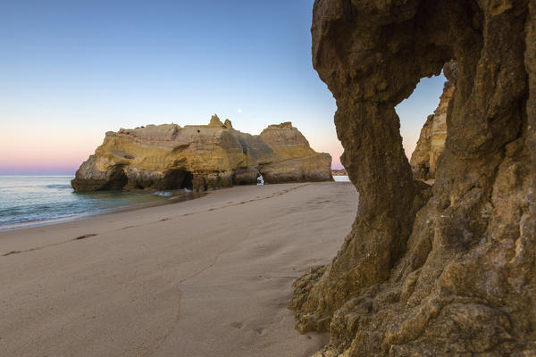 Pink sky at sunrise lights up the sandy beach and cliffs of Praia da Rocha Portimao Faro district Algarve Portugal Europe