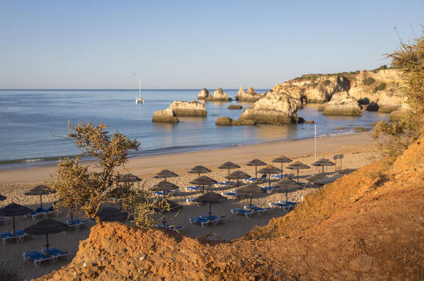 The newly risen sun shines on cliffs and bathhouse of Praia do Alemao Portimao Algarve Faro District Portugal Europe