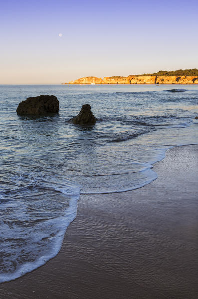 The pink sky at dawn lights up the ocean and cliffs at Praia do Vau Portimao Faro district Algarve Portugal Europe