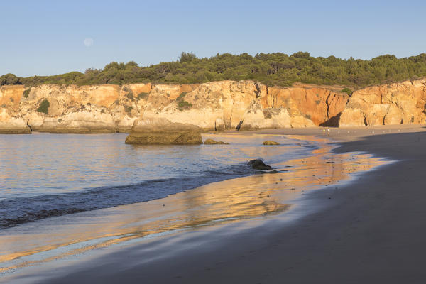 The newly risen sun shines on cliffs and reflected on the beach of Praia do Vau Algarve Faro District Portimao Portugal Europe